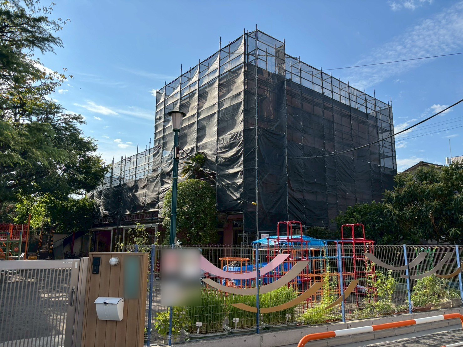 幼稚園 大規模修繕工事 施工中（足場を組み、シートで養生）